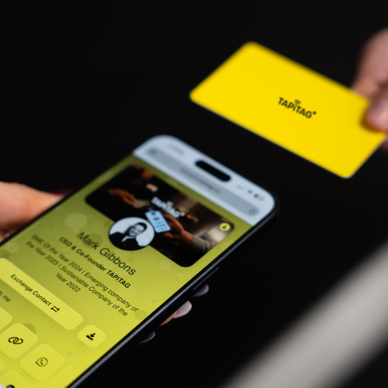 Smartphone displaying a TAPiTAG interface with a yellow Digital Business  Card in the background