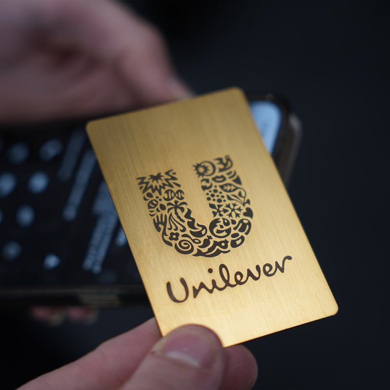 Close-up of a premium Gold TAPiTAG metal digital business card wth unileaver logo tapping a smartphone for instant contact sharing NFC
