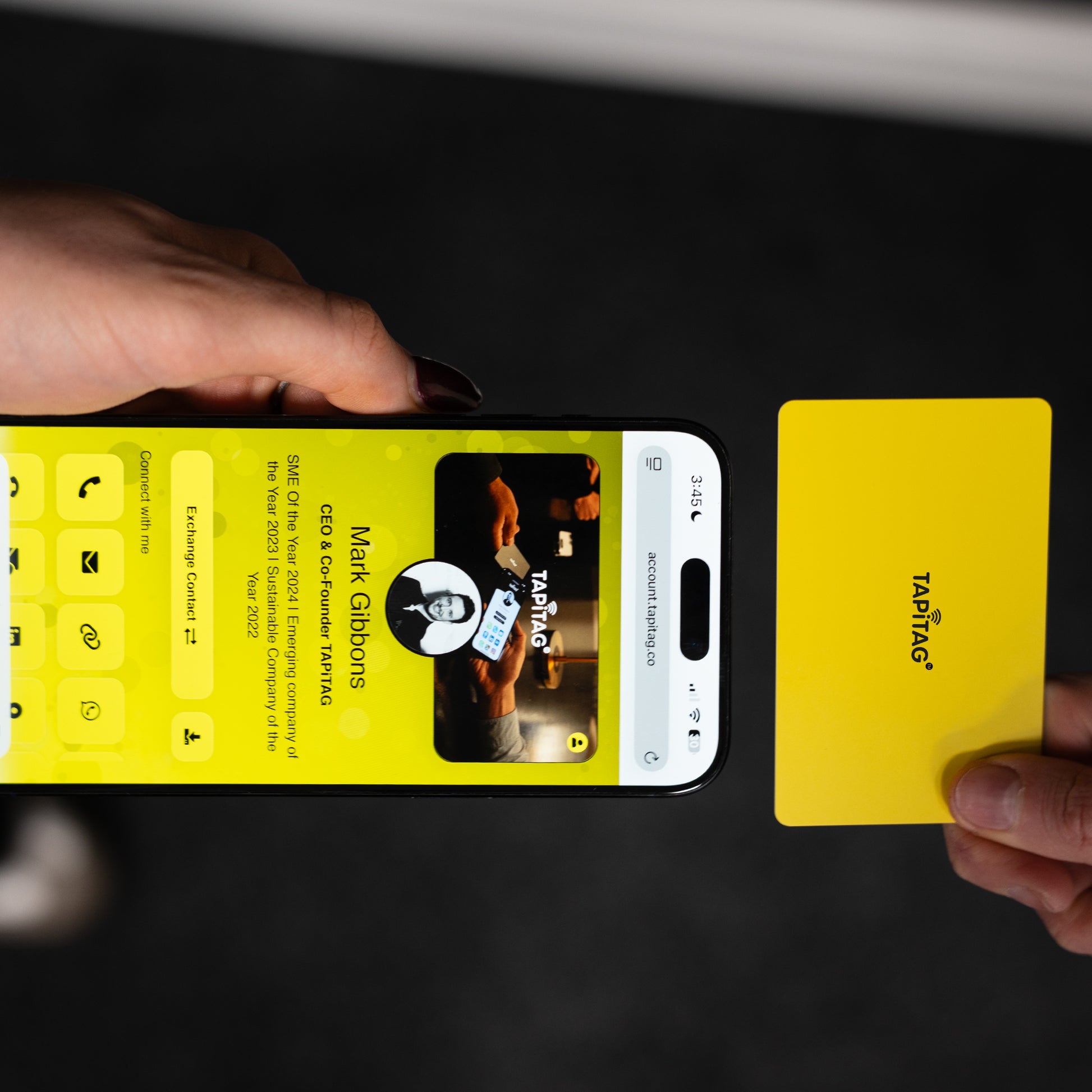 Smartphone displaying a TAPiTAG interface with a yellow Digital Business  Card in the background