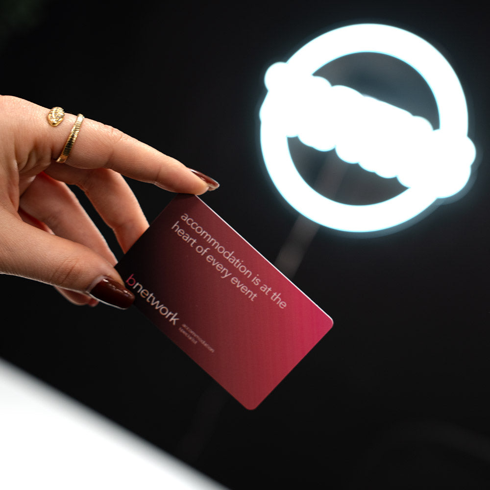 Hand holding a TAPiTAG Digital Business card  pink card with text, illuminated by a light source on a dark background