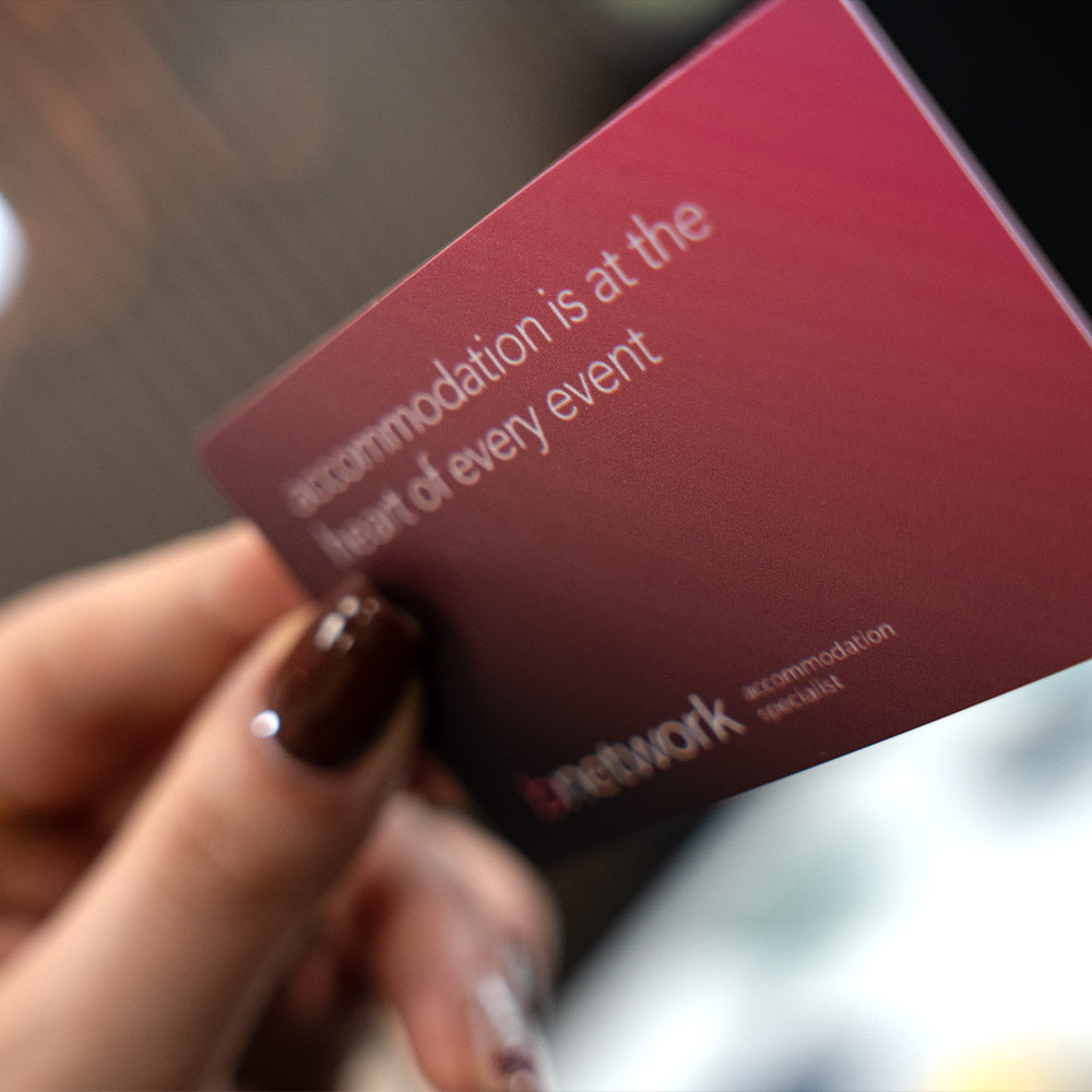 Hand holding a TAPiTAG Digital Business card  red card with text and a logo, blurred background