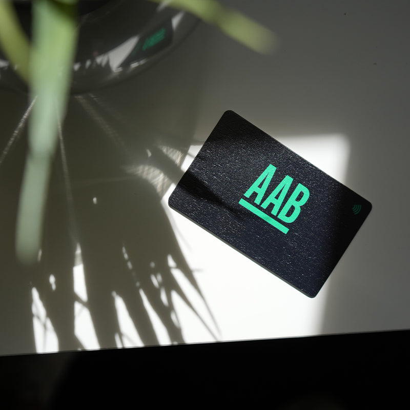 Black Bamboo NFC card with 'AAB' in green on a reflective surface with plant shadows