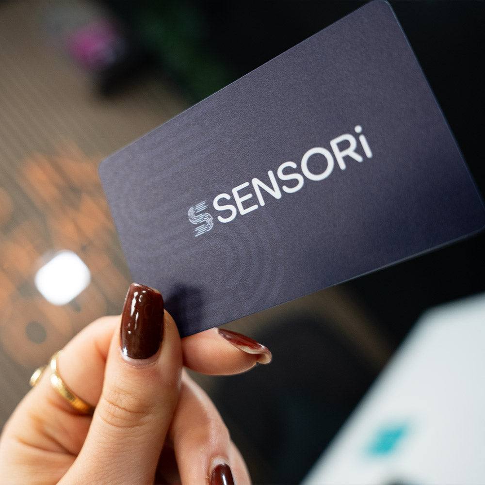 Hand holding a TAPiTAG Digital Business card  with 'SENSORI' logo against a blurred background