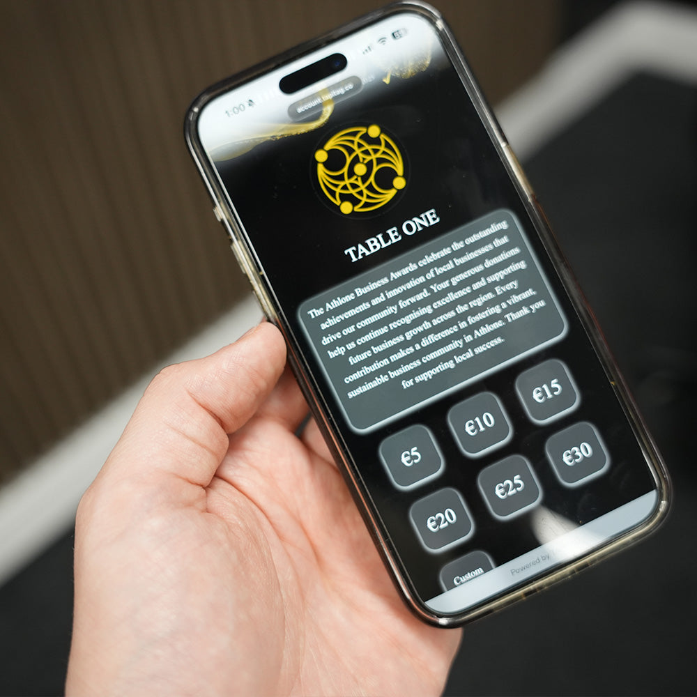 Hand holding a smartphone displaying a TAPiTAG Donations digital table menu with a logo and text.
