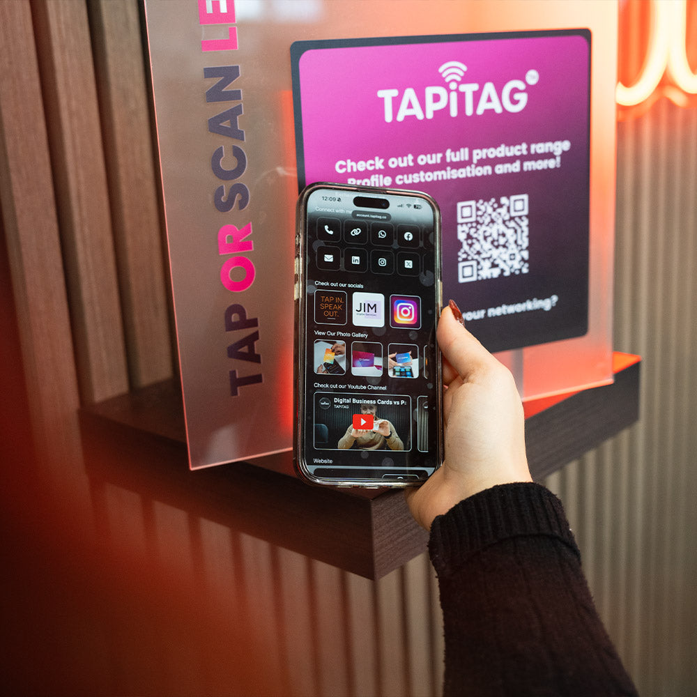 Hand holding a phone to scan a QR code on a Tapitag display.