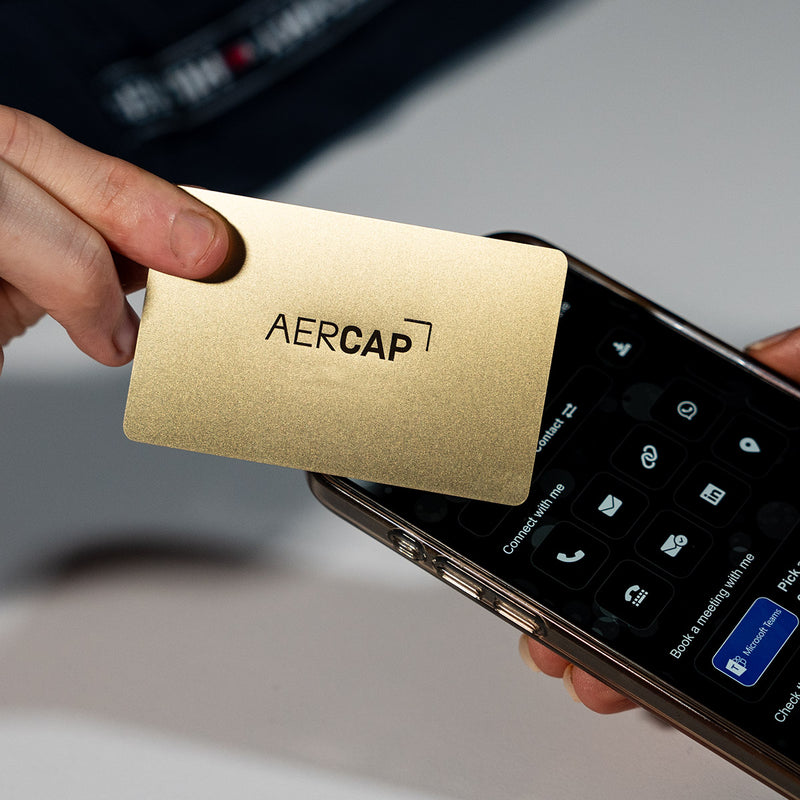 Close-up of a premium Gold TAPiTAG metal digital business card wth aercap logo tapping a smartphone for instant contact sharing NFC