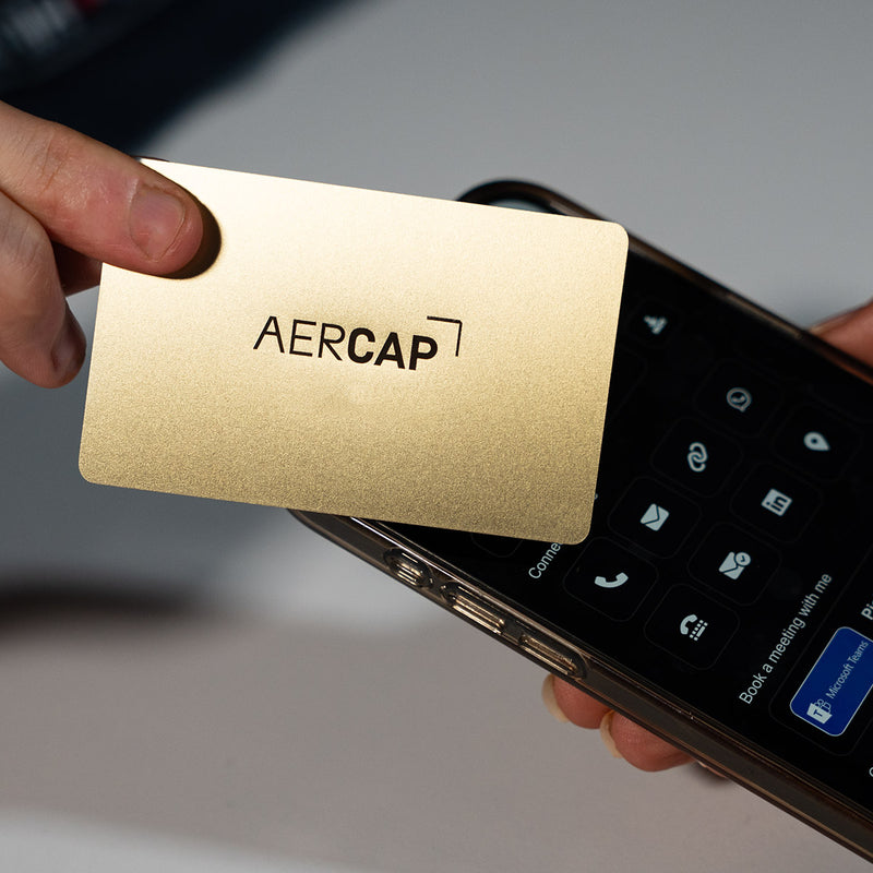 Close-up of a premium Gold TAPiTAG metal digital business card wth aercap logo tapping a smartphone for instant contact sharing NFC
