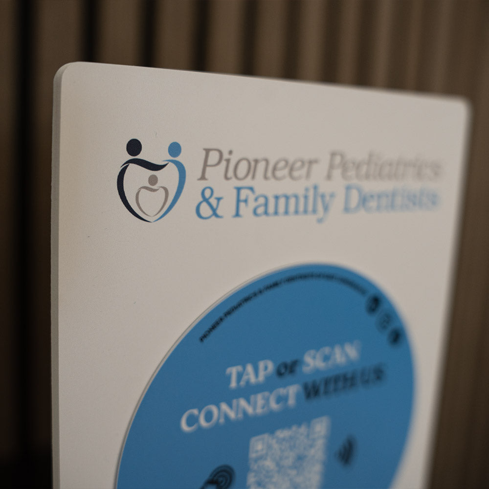 Sign for Pioneer Pediatrics & Family Dentists with a blue circle and QR code on a beige background.