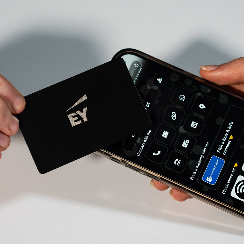 Close-up of a premium black TAPiTAG metal digital business card wth EY logo tapping a smartphone for instant contact sharing NFC