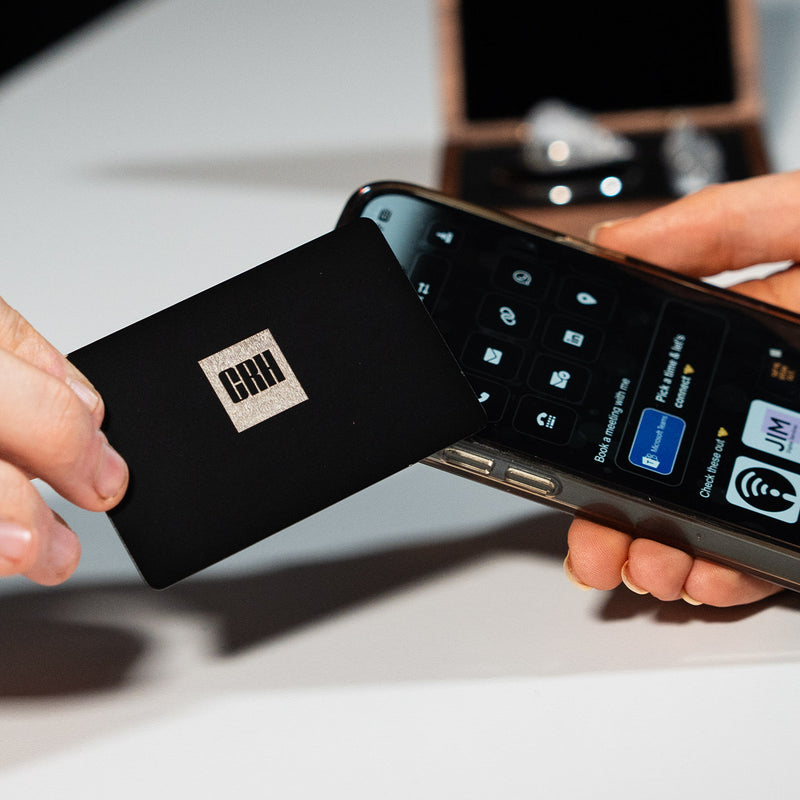 Close-up of a premium black TAPiTAG metal digital business card wth CRH tapping a smartphone for instant contact sharing NFC