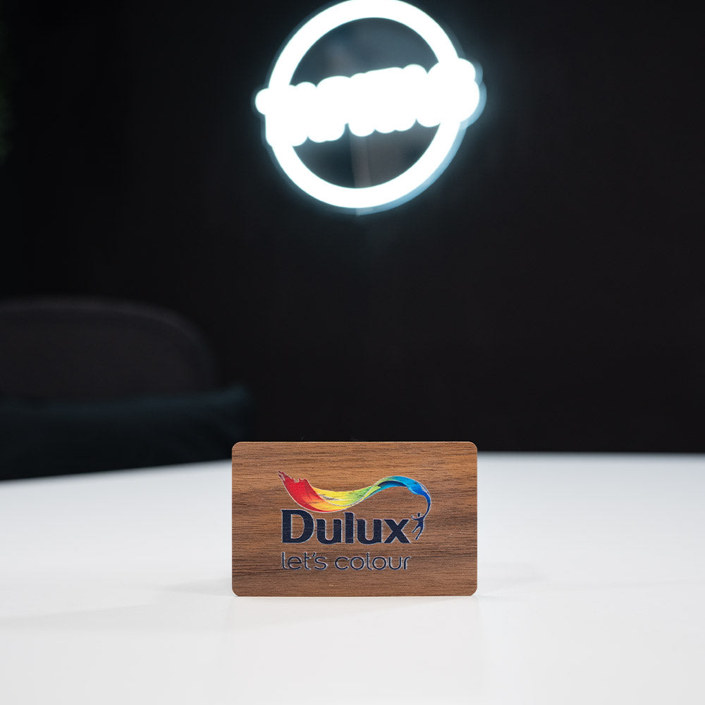 walnut Wooden Digital Business Card, also known as an NFC Business Card with Dulux branded card with a neon light in the background