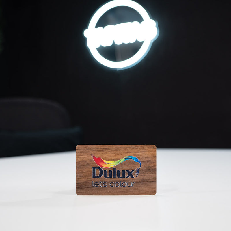 walnut Wooden Digital Business Card, also known as an NFC Business Card with Dulux branded card with a neon light in the background