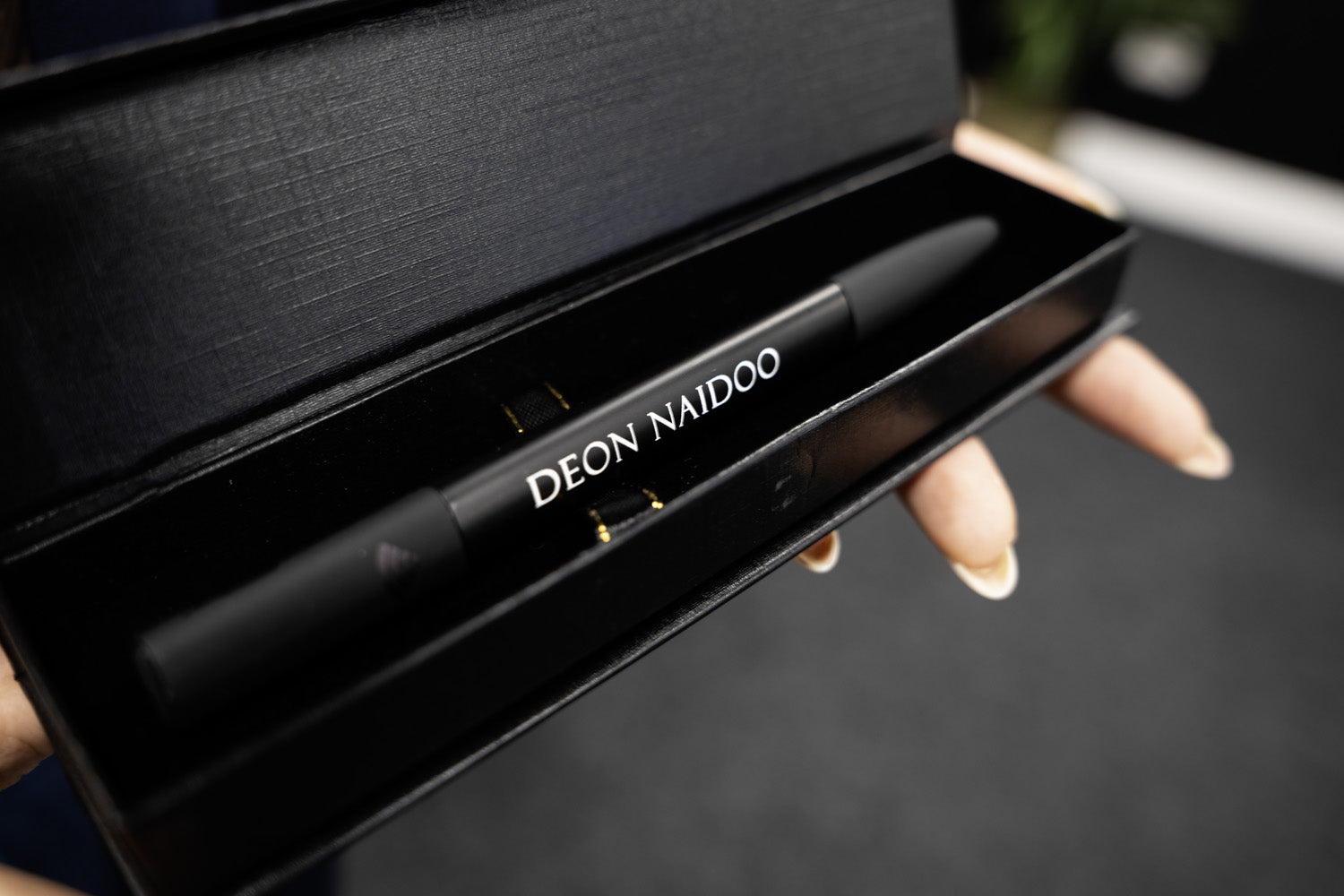 Person holding a smartphone with a contact card displayed on the screen. Phone is being held against a TAPiTAG Smart pen.