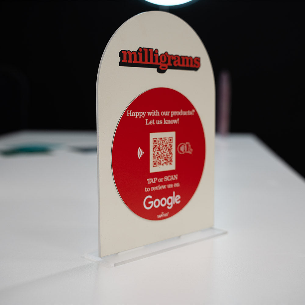 Promotional TAPiTAG Acrylic A5 ARCH display stand sign for milligrams on a wooden shelf with a blurred background. NFC TAG & QR Code.