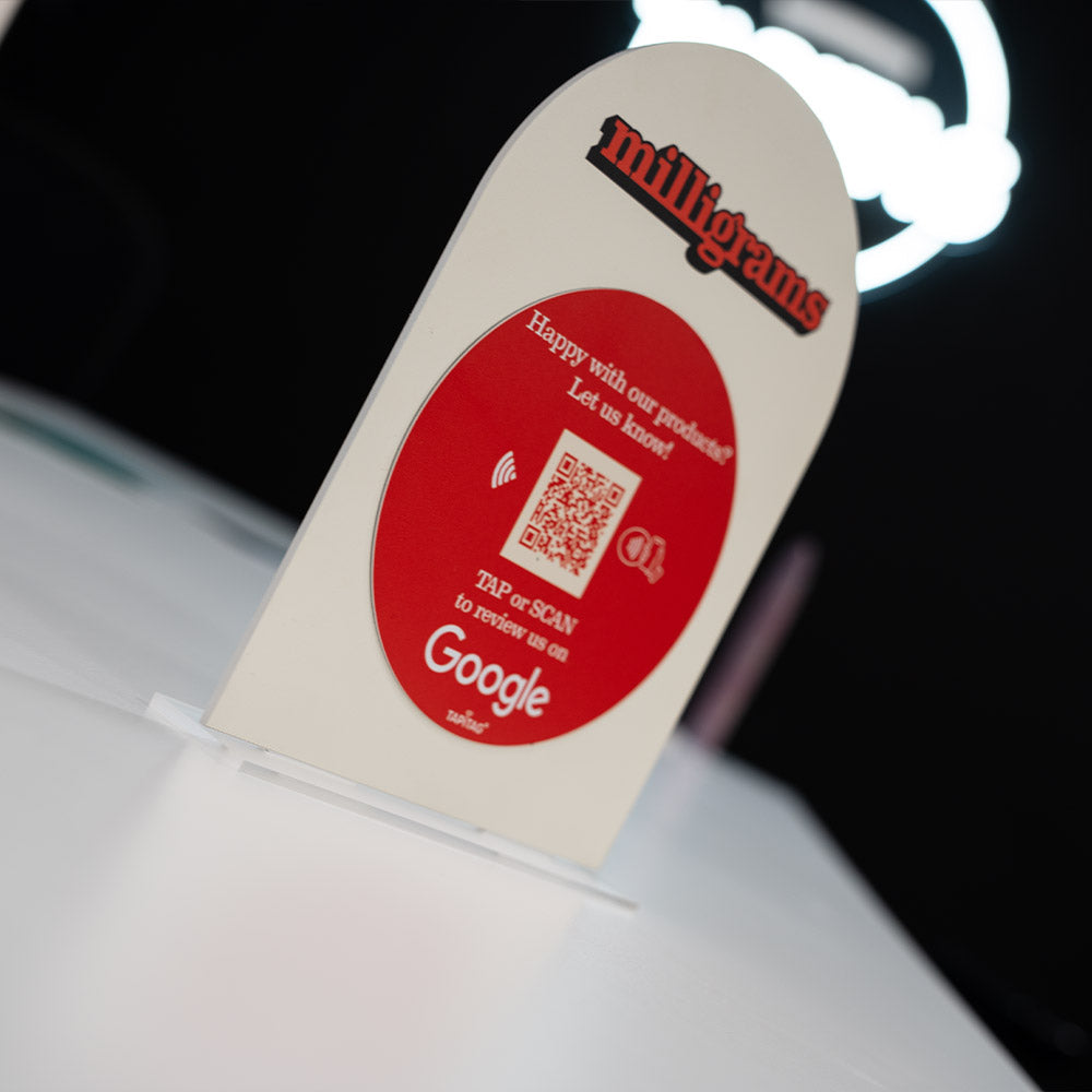 Promotional TAPiTAG Acrylic A5 ARCH display stand sign for milligrams on a wooden shelf with a blurred background. NFC TAG & QR Code.