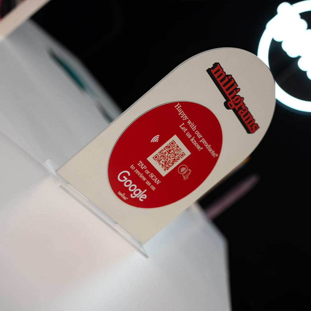 Promotional TAPiTAG Acrylic A5 ARCH display stand sign for milligrams on a wooden shelf with a blurred background. NFC TAG & QR Code.