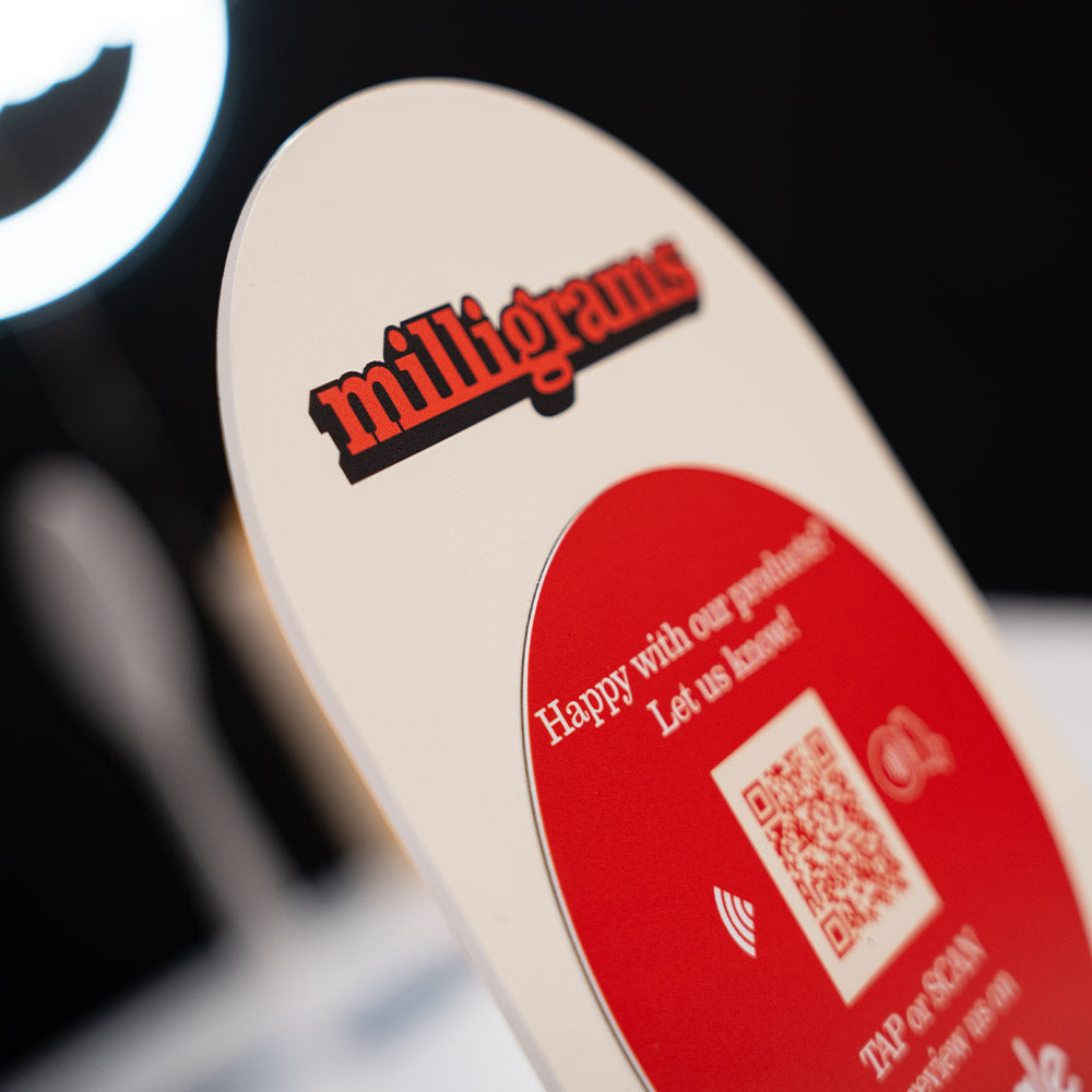 Promotional TAPiTAG Acrylic A5 ARCH display stand sign for milligrams on a wooden shelf with a blurred background. NFC TAG & QR Code.