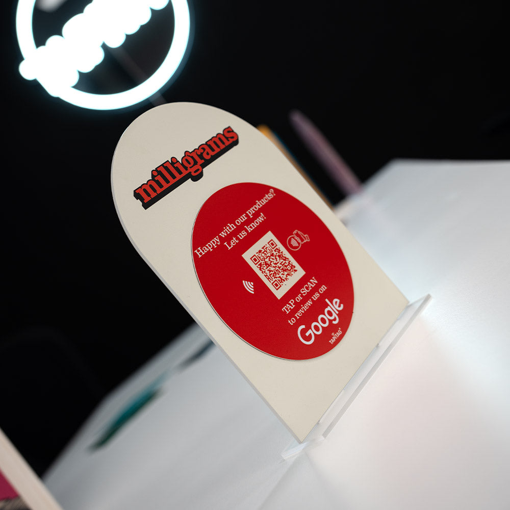 Promotional TAPiTAG Acrylic A5 ARCH display stand sign for milligrams on a wooden shelf with a blurred background. NFC TAG & QR Code.