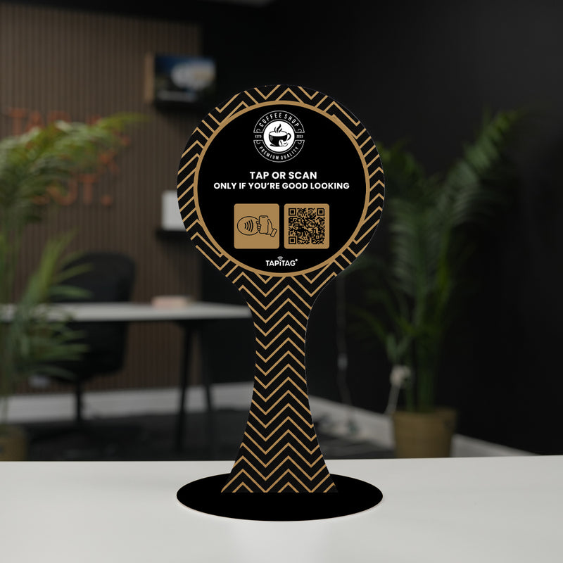 table sign with COFFEE and Google logos on a wooden table with plants in the background Decorative stand with branding and QR code on a blurred indoor background