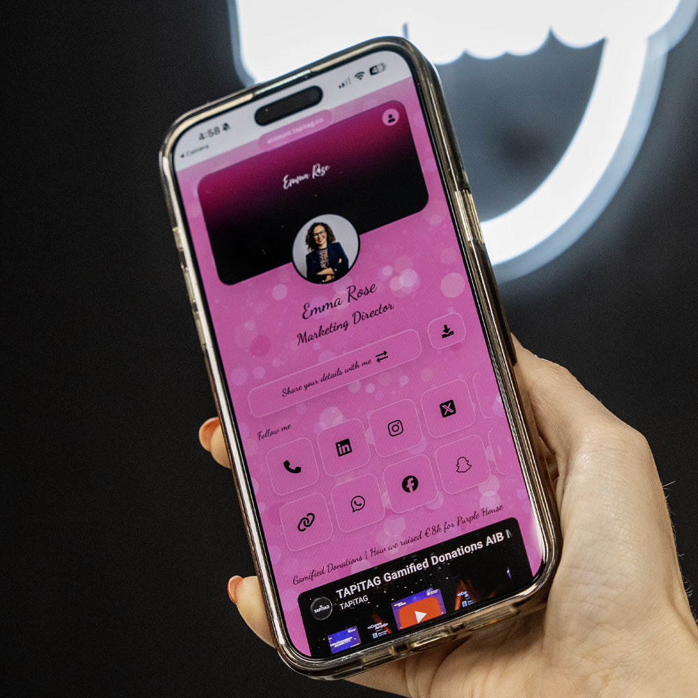Phone with a pink profile screen held by a hand against a dark background TAPiTAG Digital Business Card 