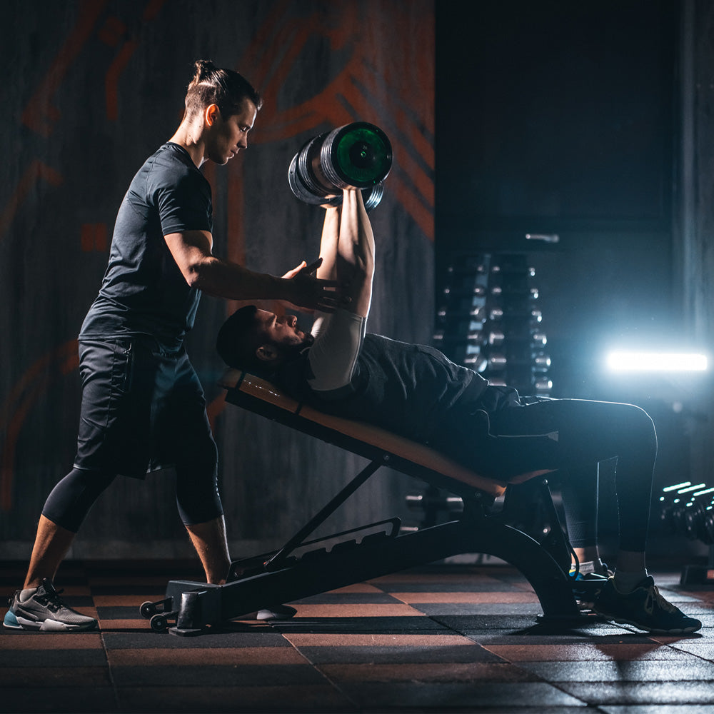 Personal trainer helping a client do a dumbbell bench press in a gym