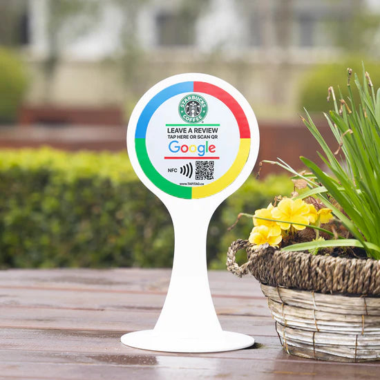 Outdoor table sign with Starbucks and Google logos on a wooden table with plants in the background