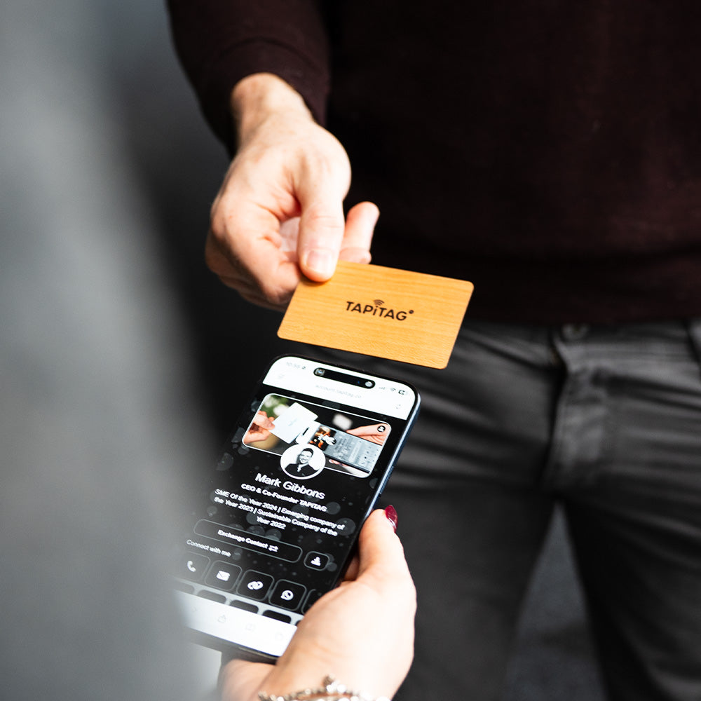 Smartphone displaying a TAPiTAG interface with a Cherry Wood Digital Business  Card in the background