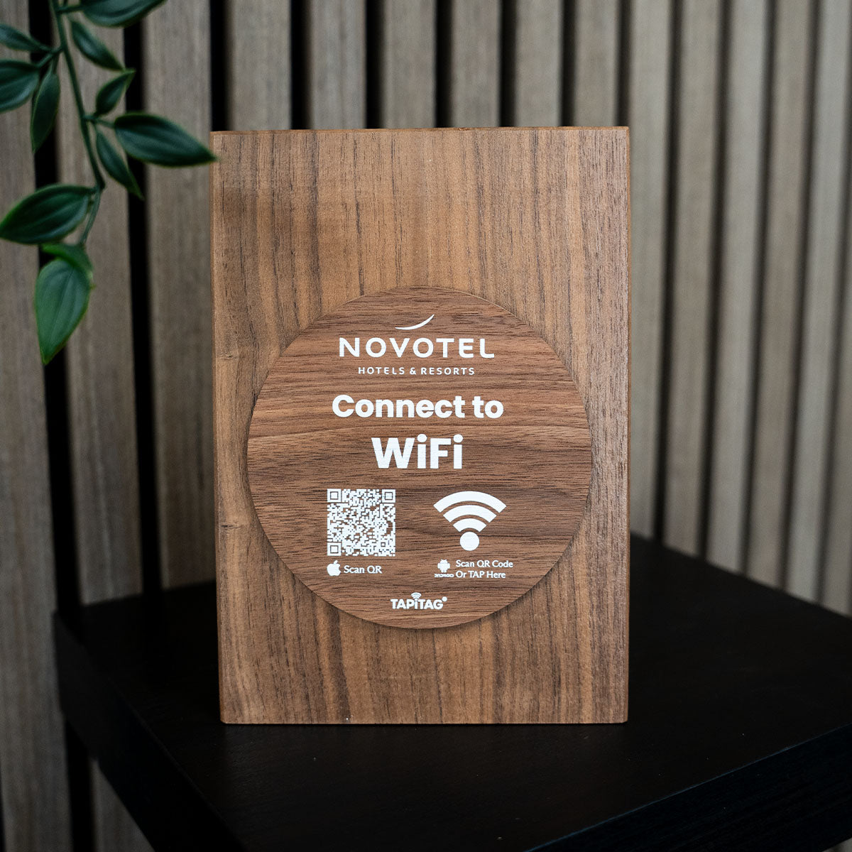  TAPiTAG wifi porter Wooden WiFi sign for Novotel hotels with QR code and Wi-Fi symbol on a wooden surface.