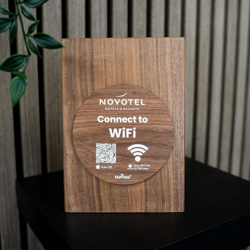  TAPiTAG wifi porter Wooden WiFi sign for Novotel hotels with QR code and Wi-Fi symbol on a wooden surface.