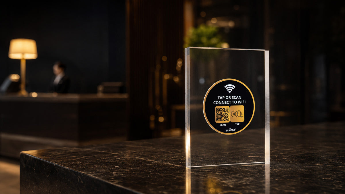 A clear acrylic TAPiTAG  nfc & QR code Wi-Fi hotspot sign on a dark marble counter in a dimly lit hotel lobby.