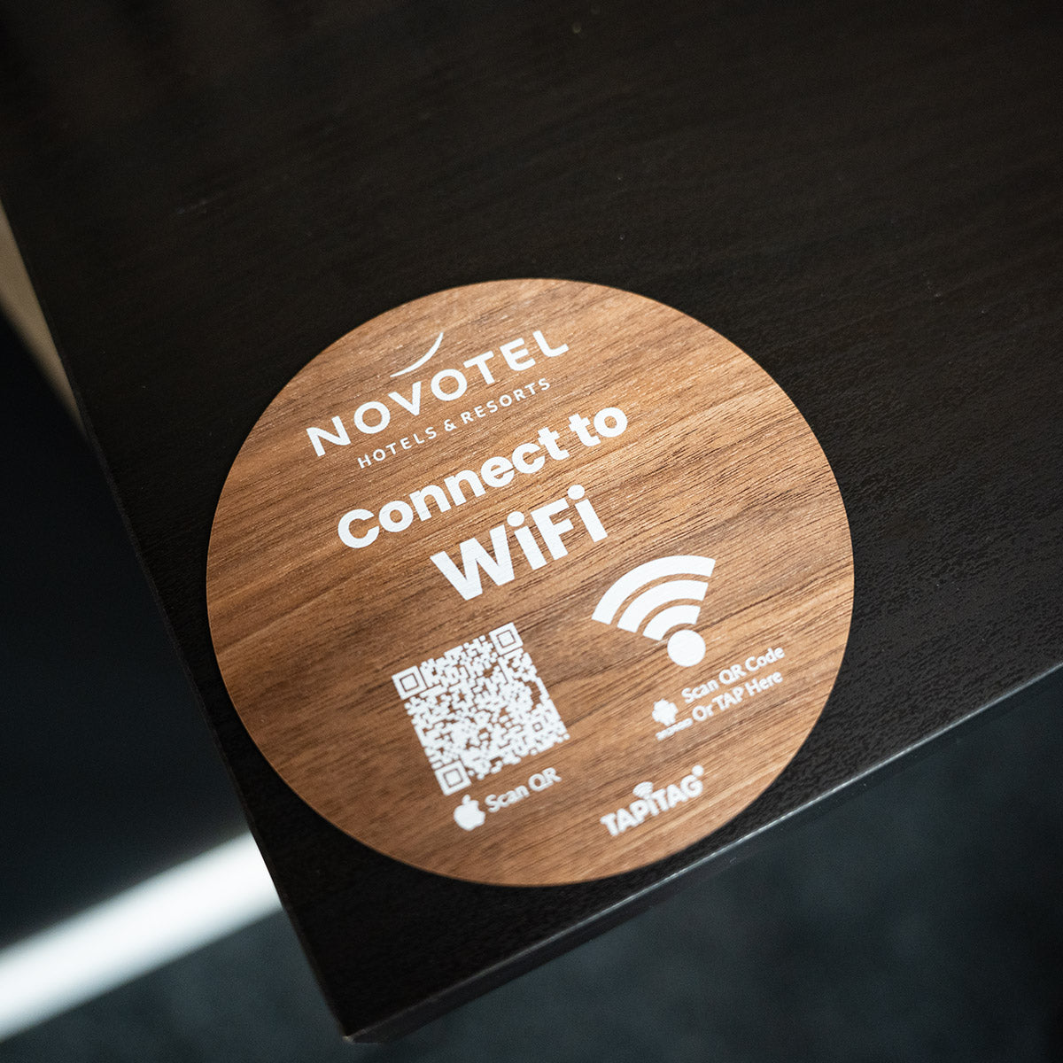  TAPiTAG wifi porter Wooden WiFi connection sign for Novotel hotels on a dark surface