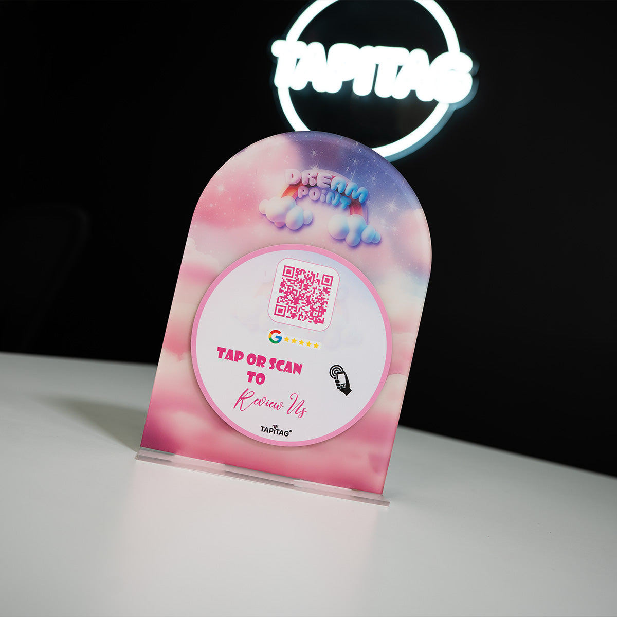 Hand holding a smartphone showing a Google review screen after tapping a TAPiTAG NFC stand on a restaurant counter, prompting customers to leave a 5-star review.