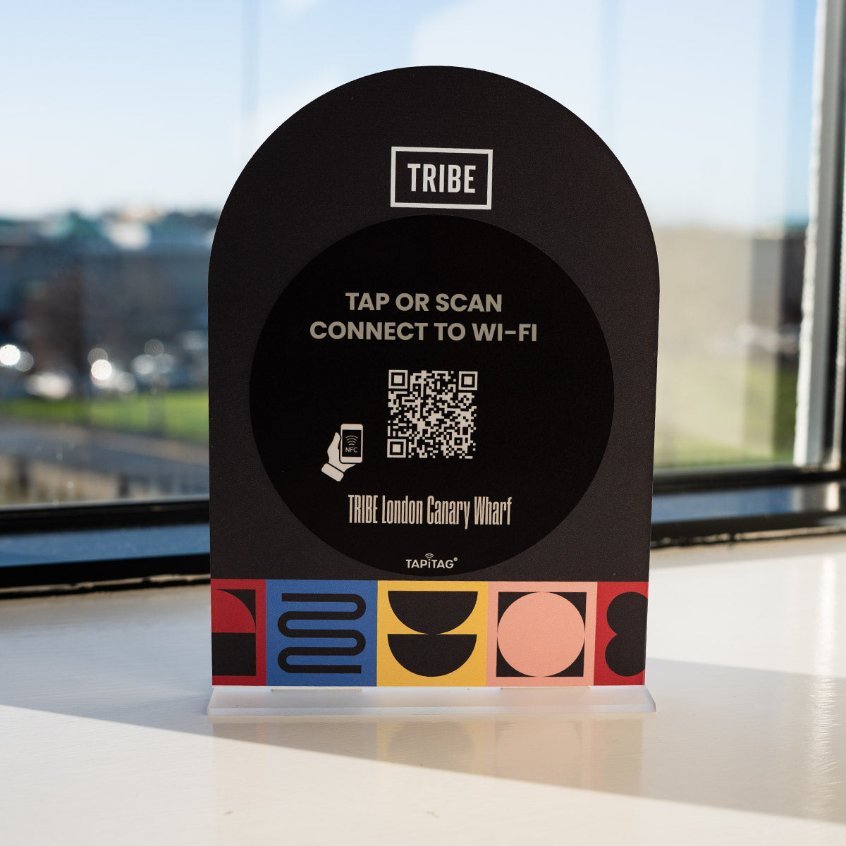 Black TAPITAG Wi-Fi PORTER connection device with QR code and 'TRIBE' branding on a surface with a blurred outdoor background.