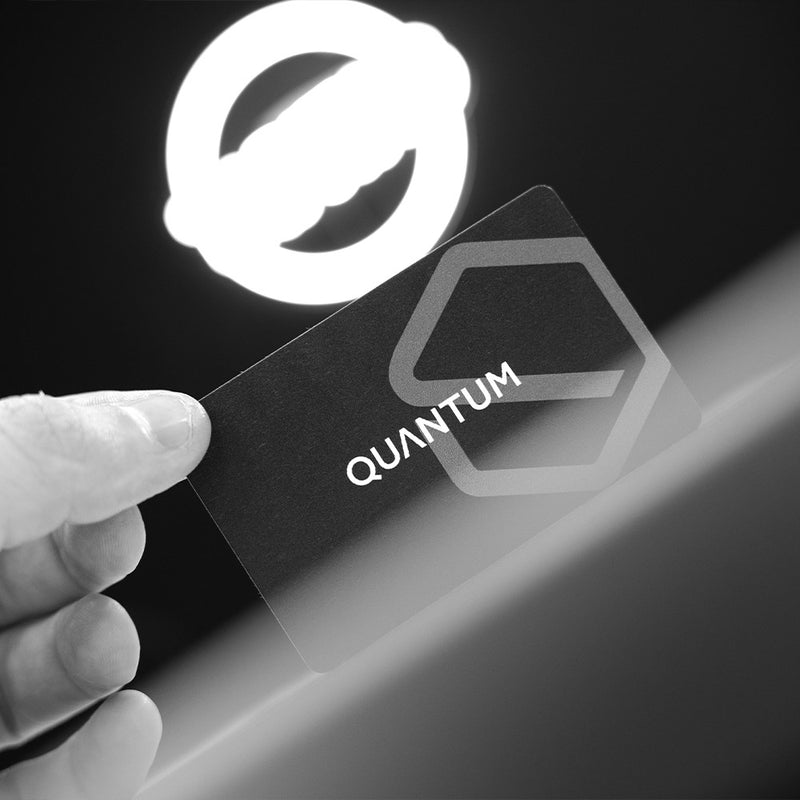 Hand holding a black card with 'QUANTUM' logo against a dark background. TAPiTAG Digital Business Card Bamboo