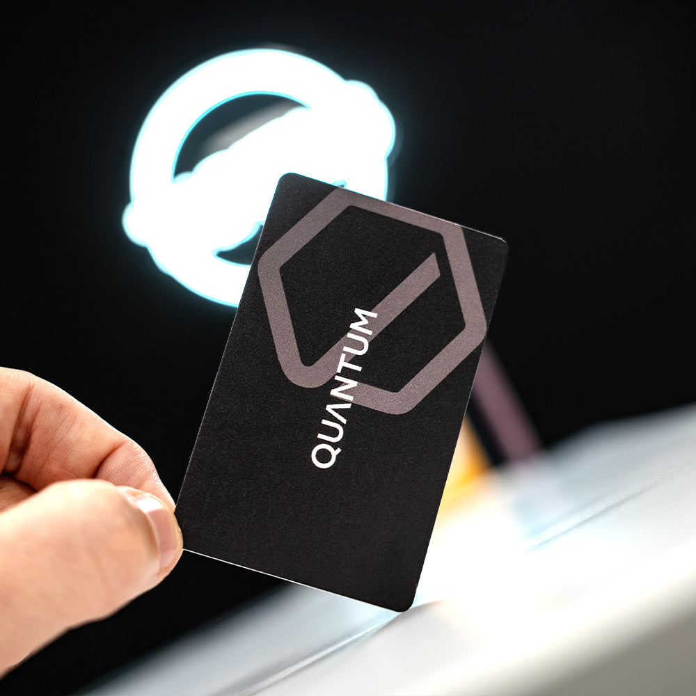 Black card with 'QUANTUM' logo held by a hand in front of a glowing 'QUANTUM' logo. TAPiTAG Digital Business Card Bamboo