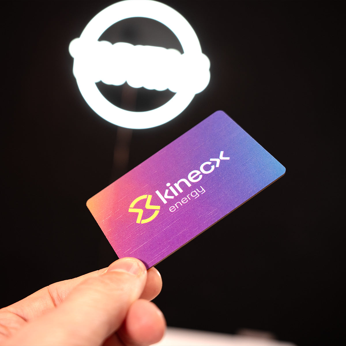 Hand holding a Kinecx energy TAPiTAG Digital Business card with a logo in the background