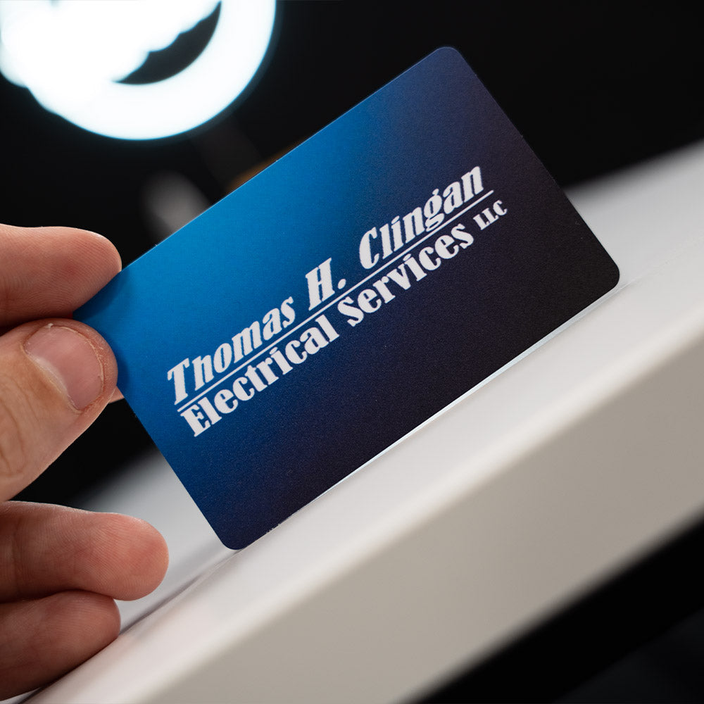 blue TAPiTAG NFC-Enabled Digital Business Card  Hand holding a blue business card with 'Thomas H. Clingan Electrical Services LLC' text.