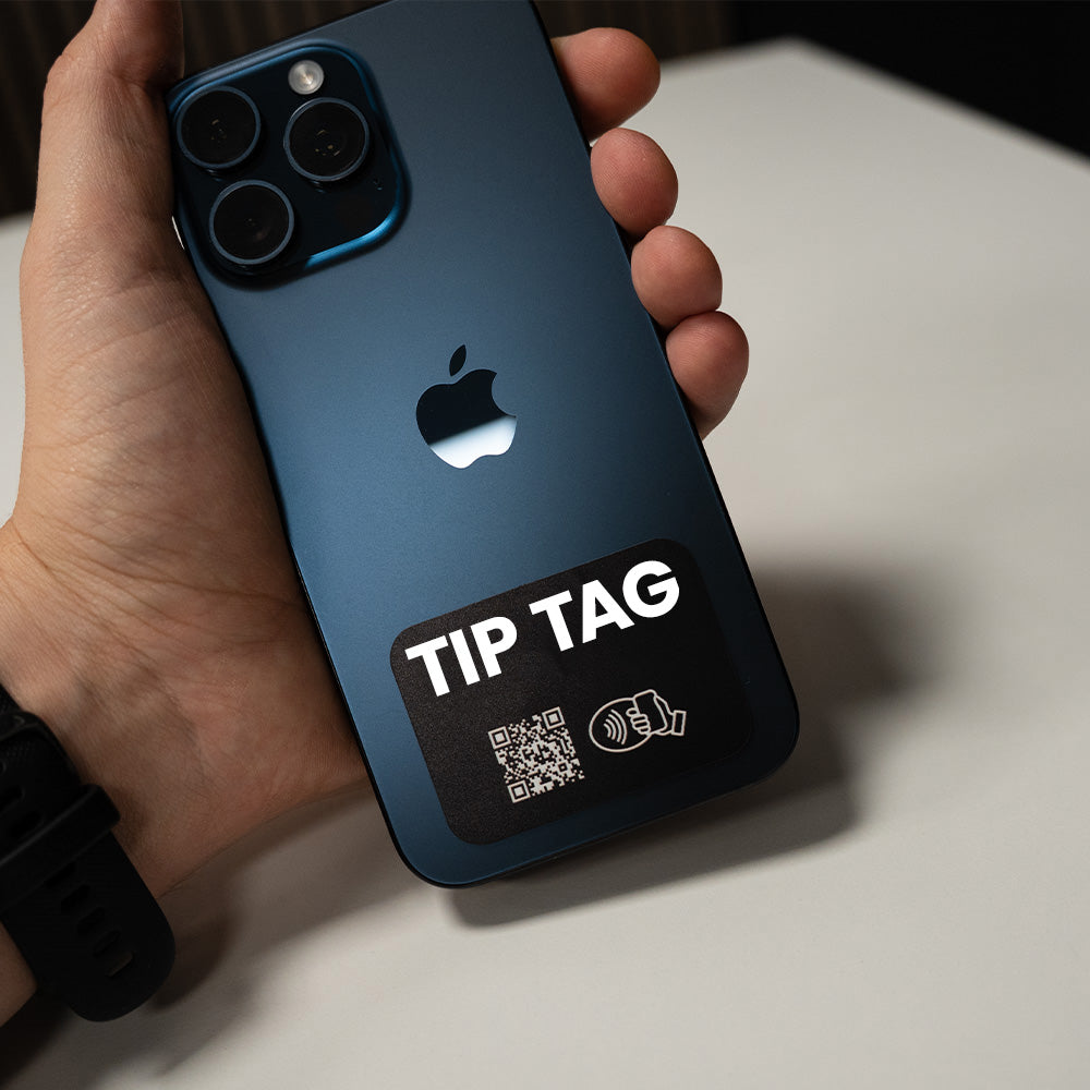 Hand holding a blue smartphone with a 'TIP TAG' label on a white surface