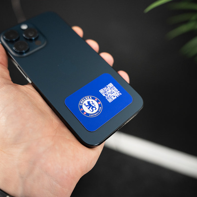Hand holding a smartphone with a Chelsea FC app icon and QR code on the screen. TAPiTAG NFC QR MINICARD NFC-Enabled Digital Business Card