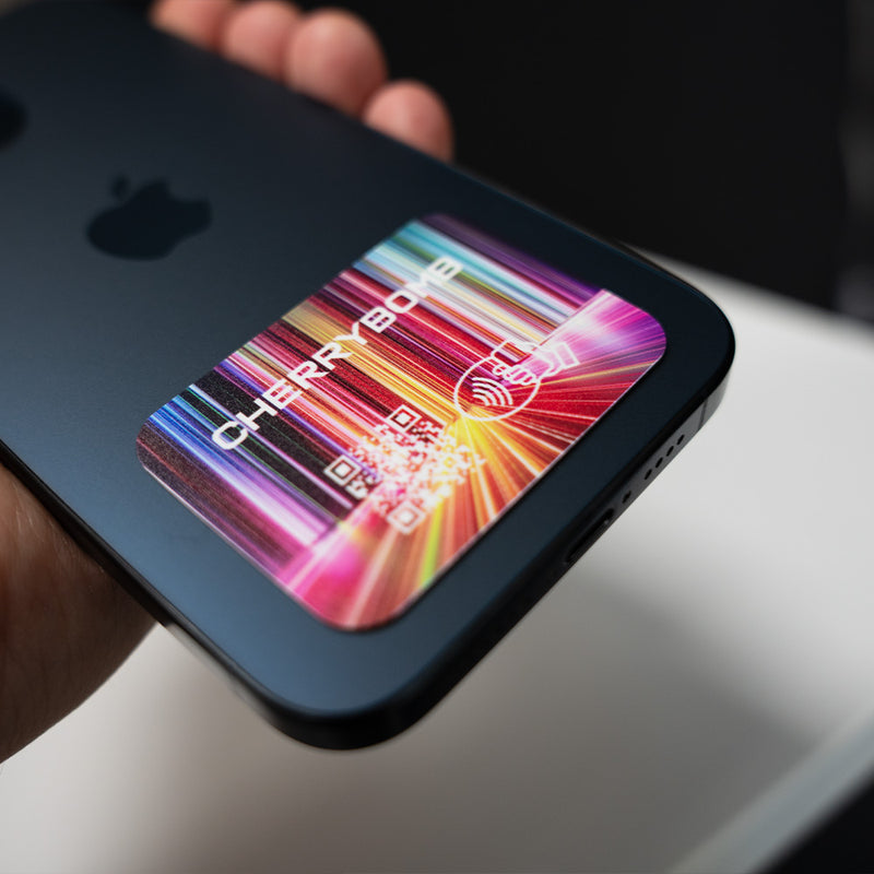 Smartphone with a colorful Cherry Bomb logo on the screen held by a person. TAPiTAG NFC QR MINICARD NFC-Enabled Digital Business Card
