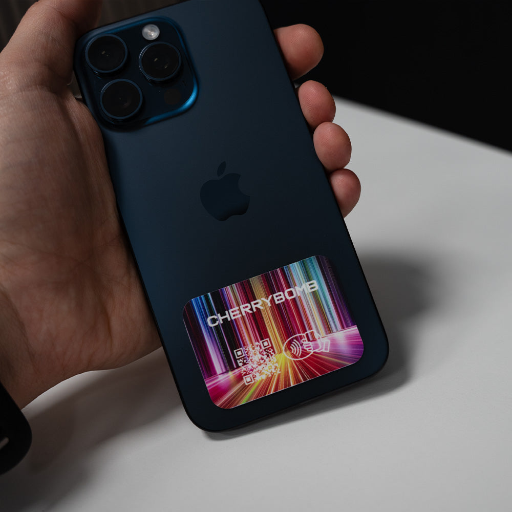 Person holding a black smartphone with a colorful Cherrybomb case on a white surface. TAPiTAG NFC QR MINICARD NFC-Enabled Digital Business Card