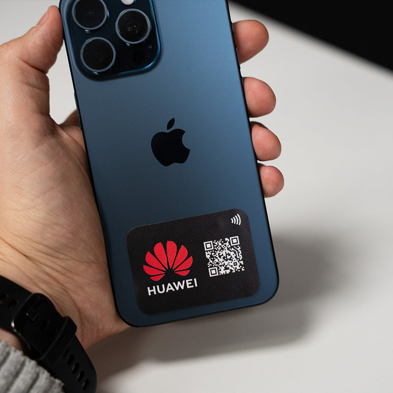 Hand holding a smartphone with a Huawei sticker featuring a QR code on a light background. TAPiTAG NFC QR MINICARD NFC-Enabled Digital Business Card
