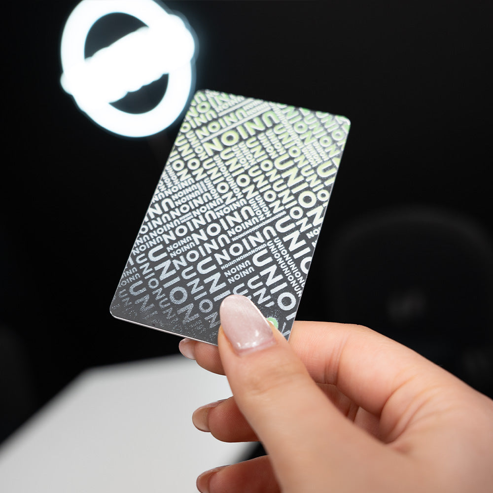 Hand holding a Mirror TAPiTAG Digital Business Card with 'UNION' printed on it against a dark background