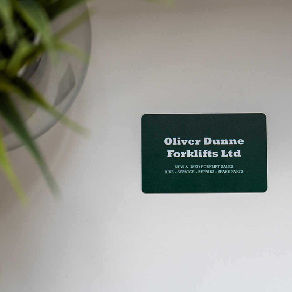 Business card for Oliver Dunne Forklifts Ltd on a white surface with a plant in the corner. Green PVC digital business card 