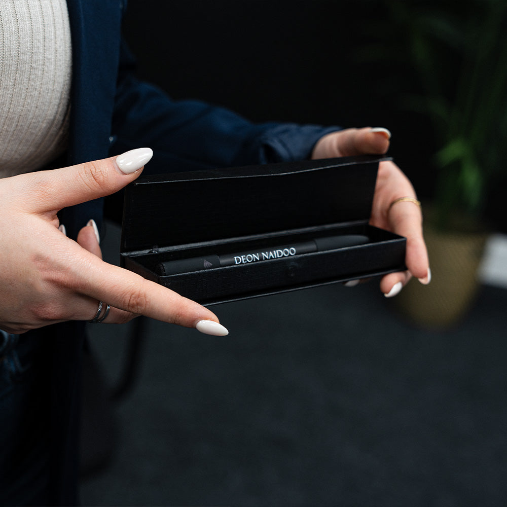 Person holding a smartphone with a contact card displayed on the screen. Phone is being held against a TAPiTAG Smart pen.