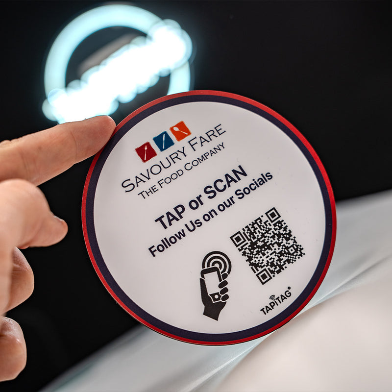 Round promotional sticker for Savoury Fare with QR code and social media prompts, held by a hand. Custom Design TAPiTAG with NFC TAG & QR Code. Designed in TAPiTAG Studio. Tag links direct to Google Reviews - TAPiTAG google review tag.