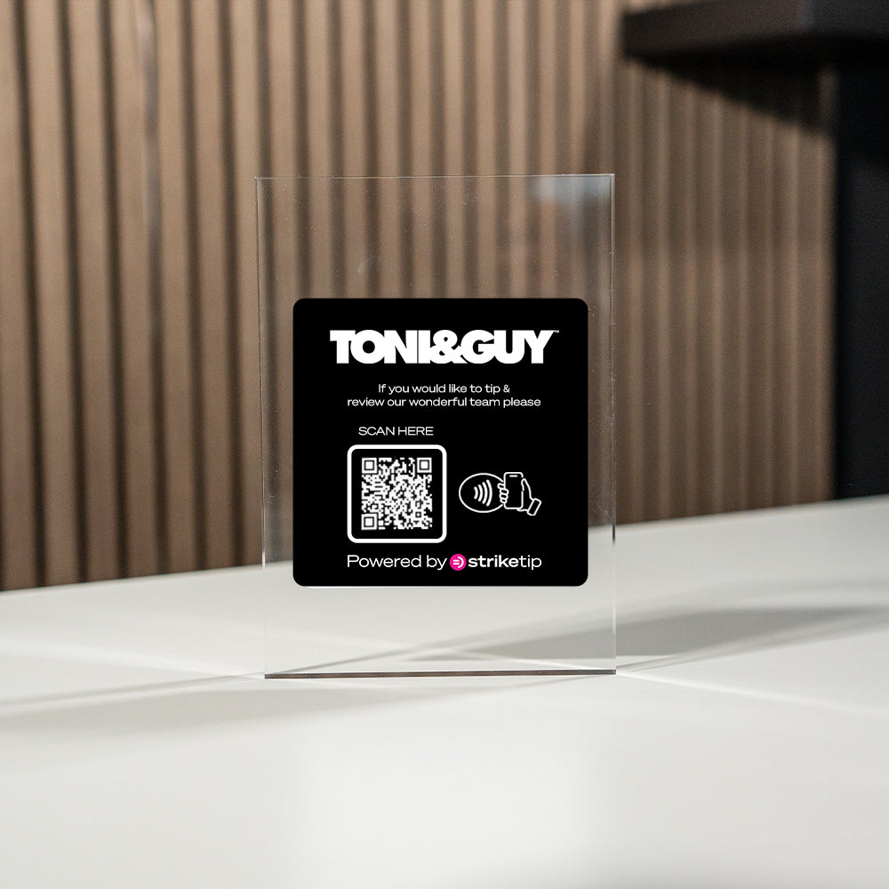 Toni&Guy tipping card with QR code on a clear TAPiTAG Display stand against a wooden wall.