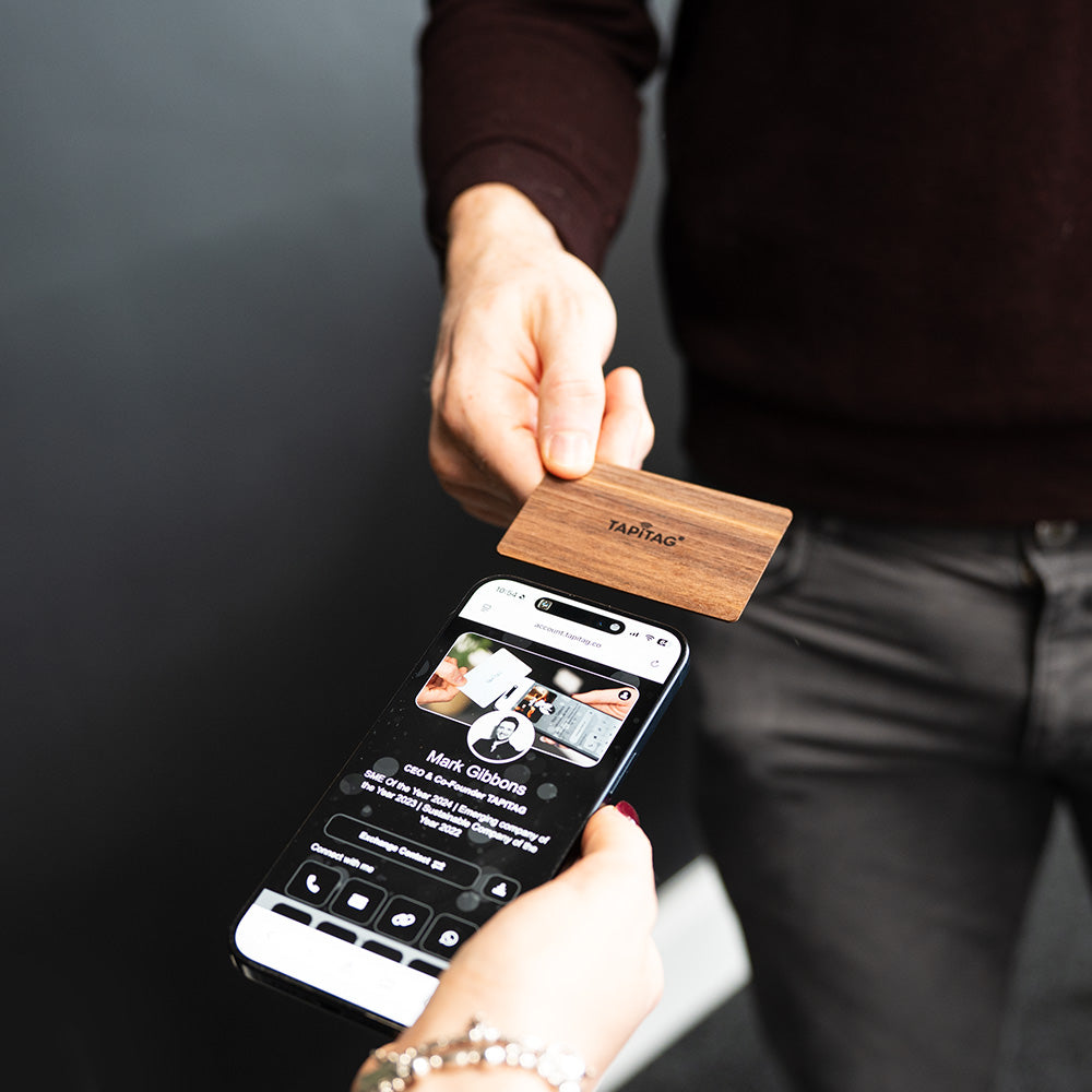 Smartphone displaying a TAPiTAG interface with a Walnut Wood Digital Business  Card in the background