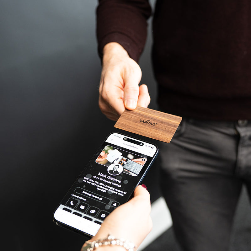 Smartphone displaying a TAPiTAG interface with a Walnut Wood Digital Business  Card in the background